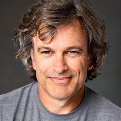 young man with longish wavy brown hair, wearing gray t-shirt and looking straight forward